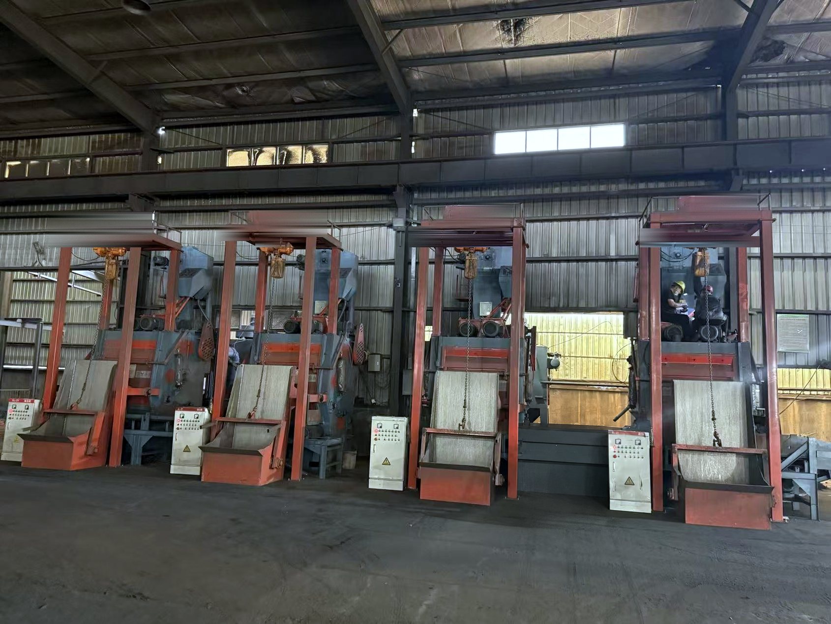 Row of tumble-belt shot blasting machines cleaning castings
